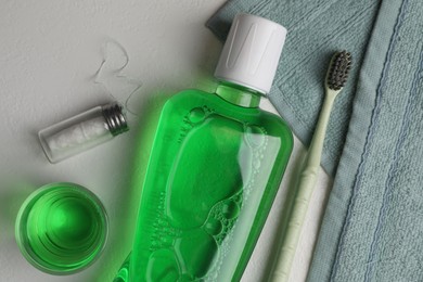 Photo of Fresh mouthwash in bottle, glass, toothbrush and dental floss on light background, flat lay