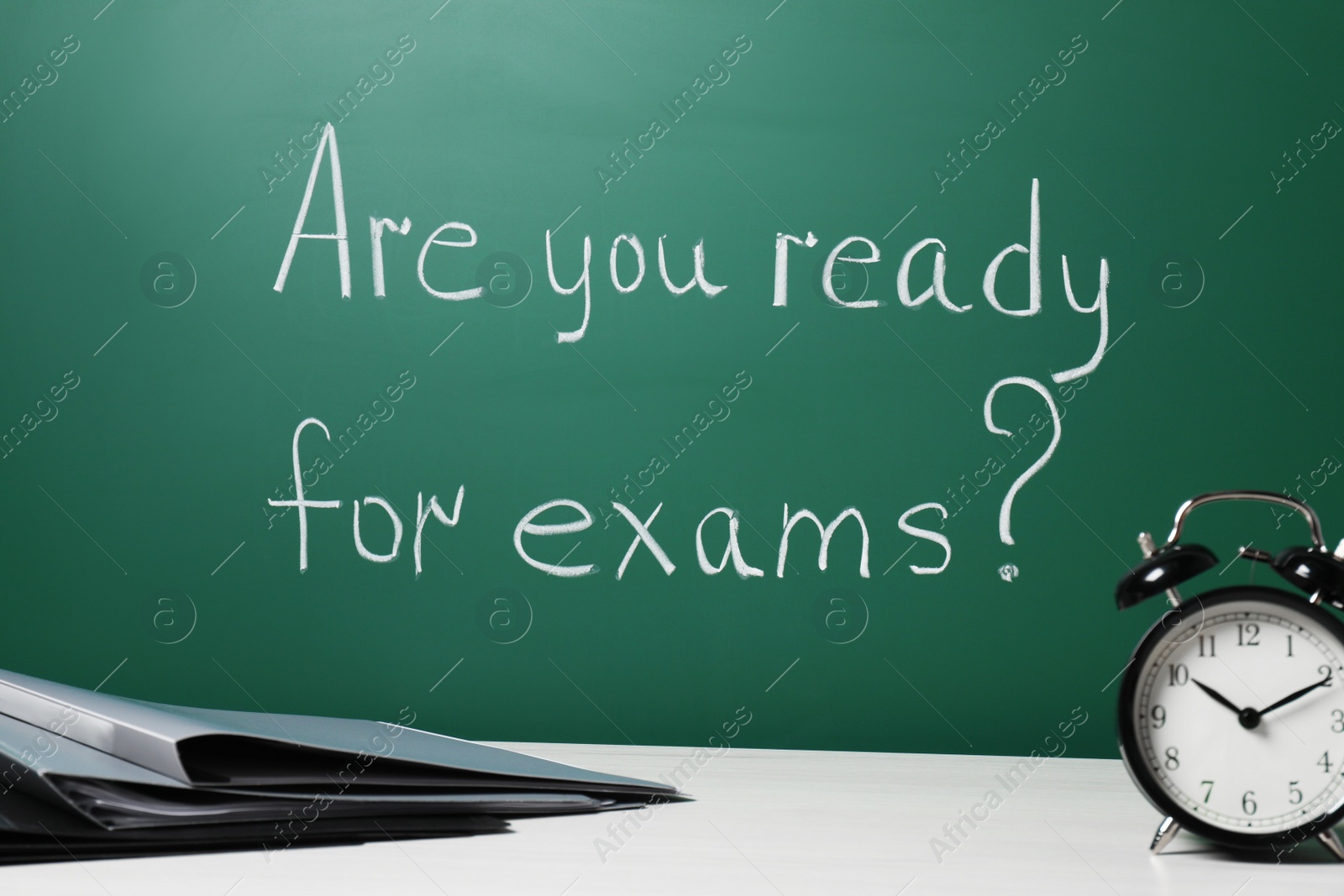 Photo of Office folders and alarm clock on white table near chalkboard with phrase Are You Ready For Exams