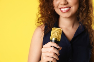 Photo of Curly African-American woman holding microphone on color background, closeup view with space for text