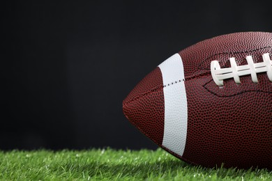 Photo of American football ball on green grass against black background, closeup. Space for text