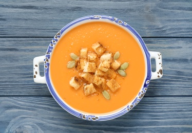 Photo of Tasty creamy pumpkin soup with croutons and seeds in bowl on blue wooden table, top view