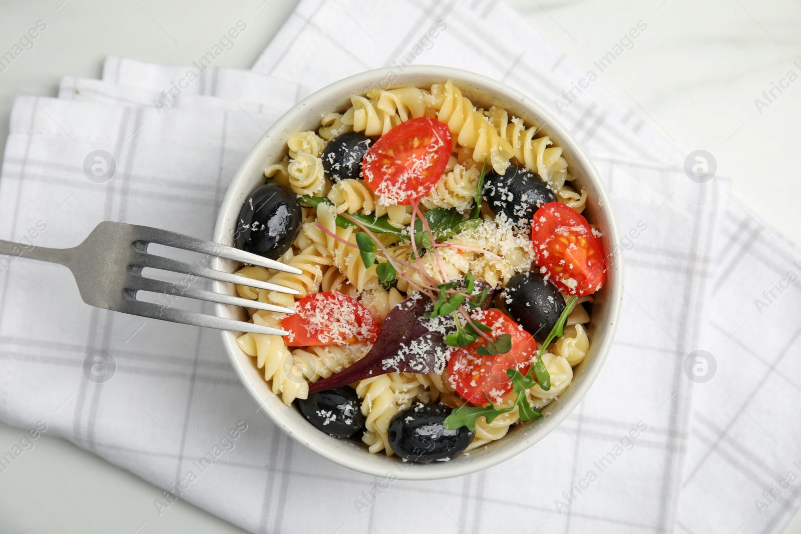 Photo of Bowl of delicious pasta with tomatoes, olives and cheese on white table, top view