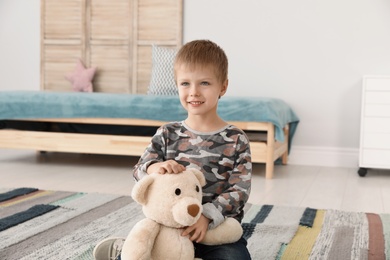 Photo of Cute little boy playing with teddy bear at home