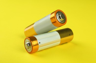 Two new AA batteries on yellow background, closeup