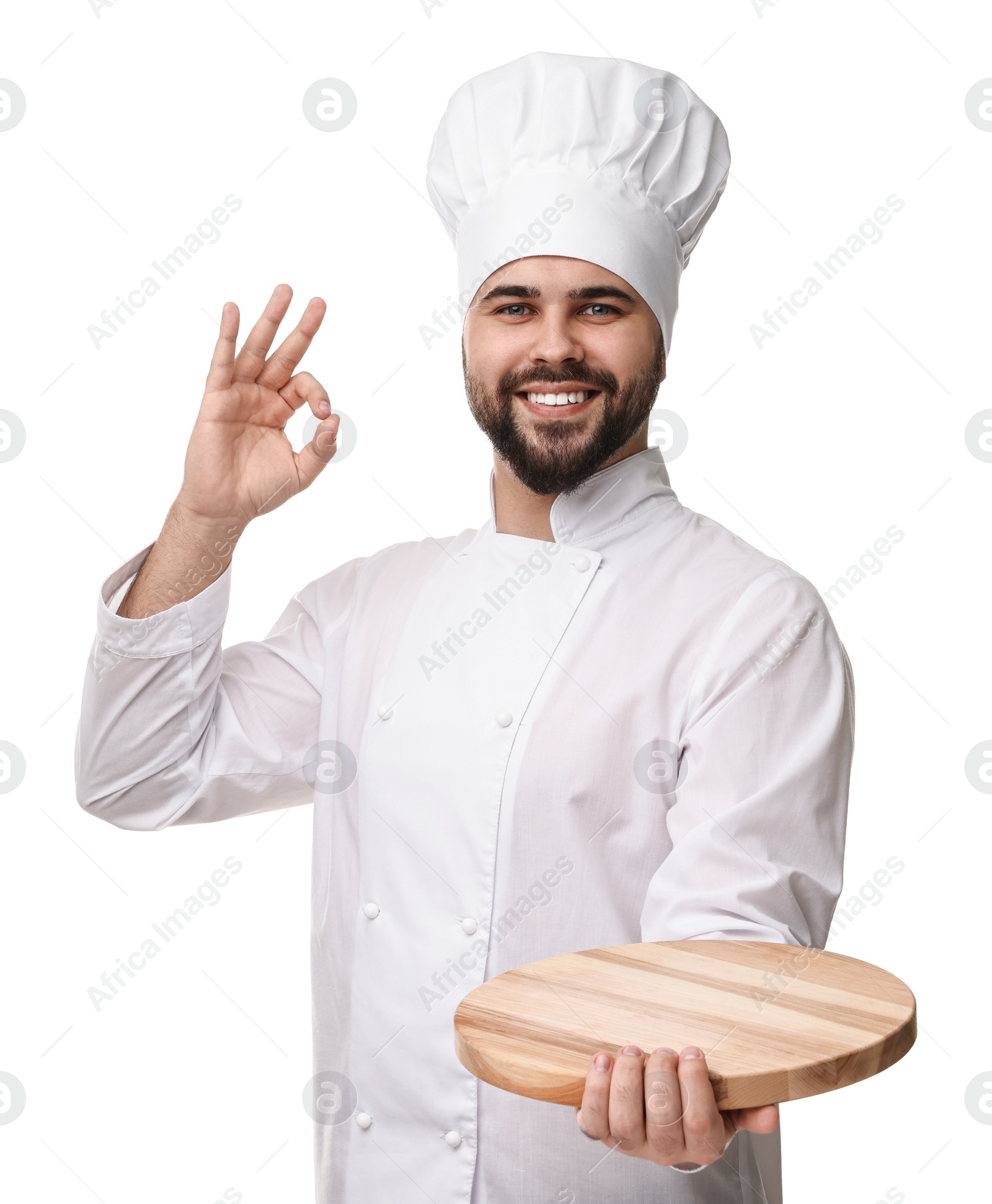 Photo of Happy young chef in uniform holding wooden board and showing ok gesture on white background