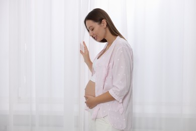 Photo of Beautiful pregnant woman in pink shirt near window indoors