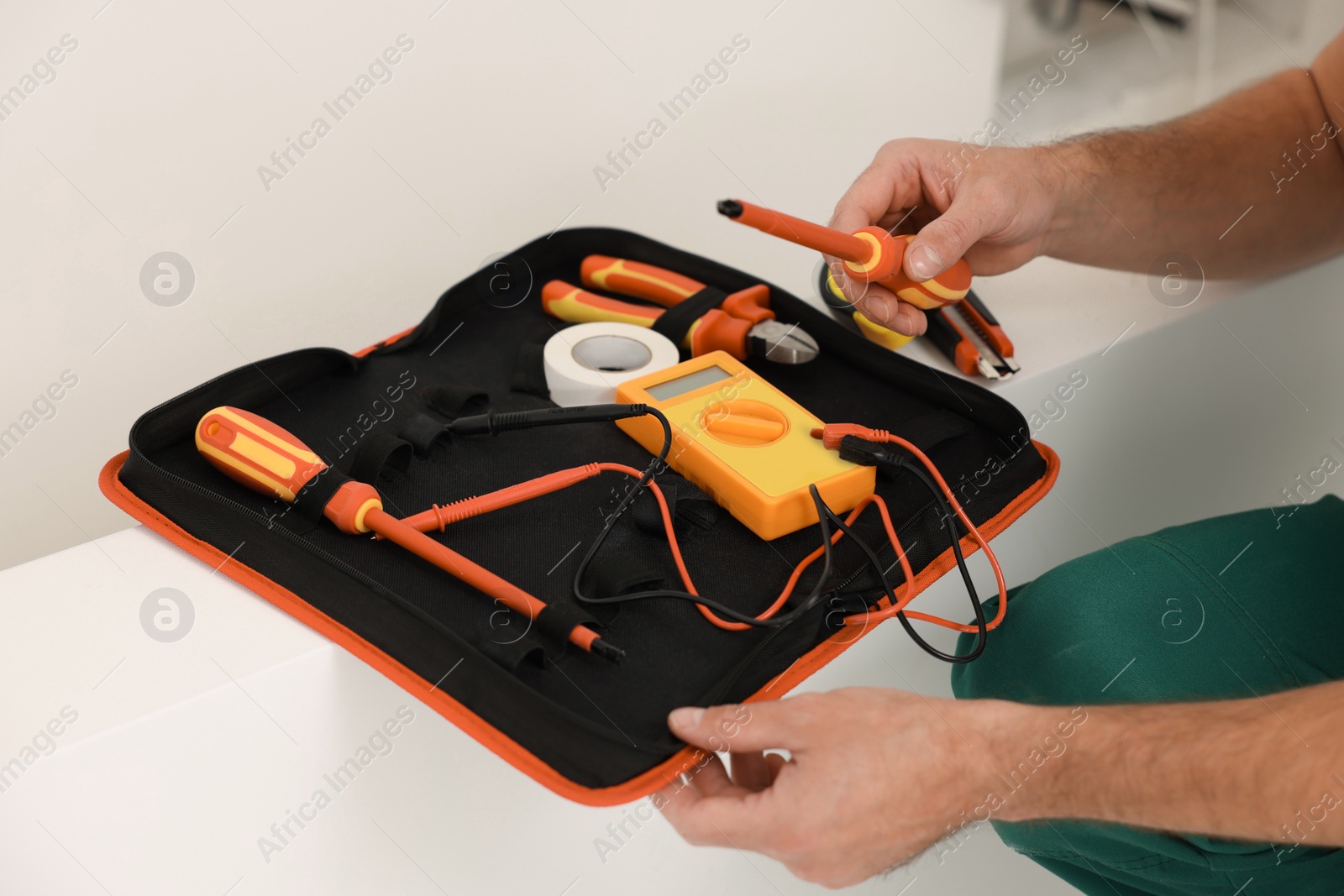 Photo of Electrician taking screwdriver from tool bag indoors, closeup