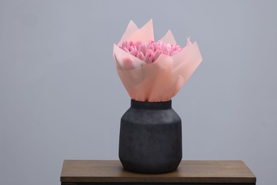 Bouquet of beautiful pink tulips in vase on wooden table against light grey background