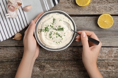 Woman preparing tasty creamy dill sauce at wooden table, top view