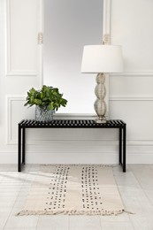 Photo of Console table with lamp, bouquet of green branches and mirror in room. Interior design