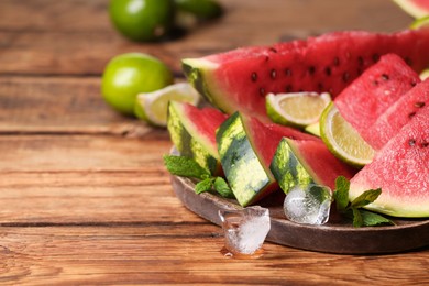 Photo of Slices of delicious ripe watermelon, ice cubes and cut lime on wooden table, space for text