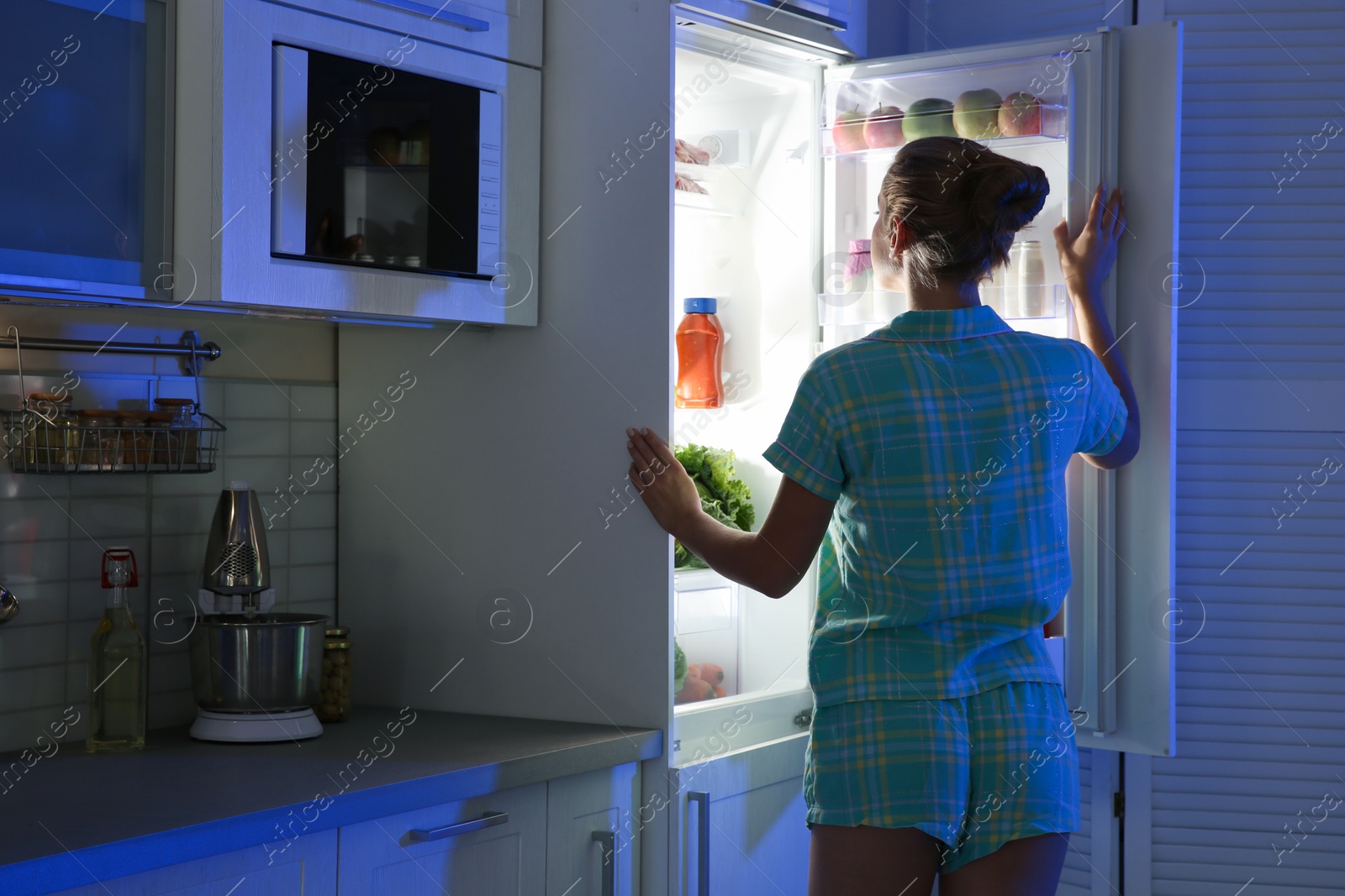 Photo of Woman choosing food from refrigerator in kitchen at night