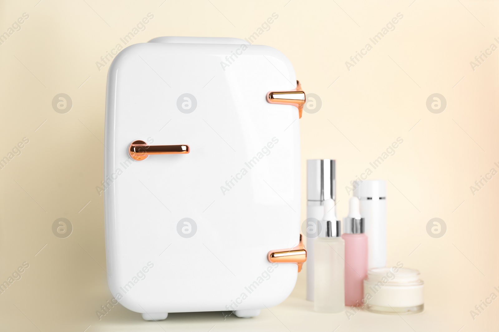 Photo of Cosmetic refrigerator and skin care products on beige background