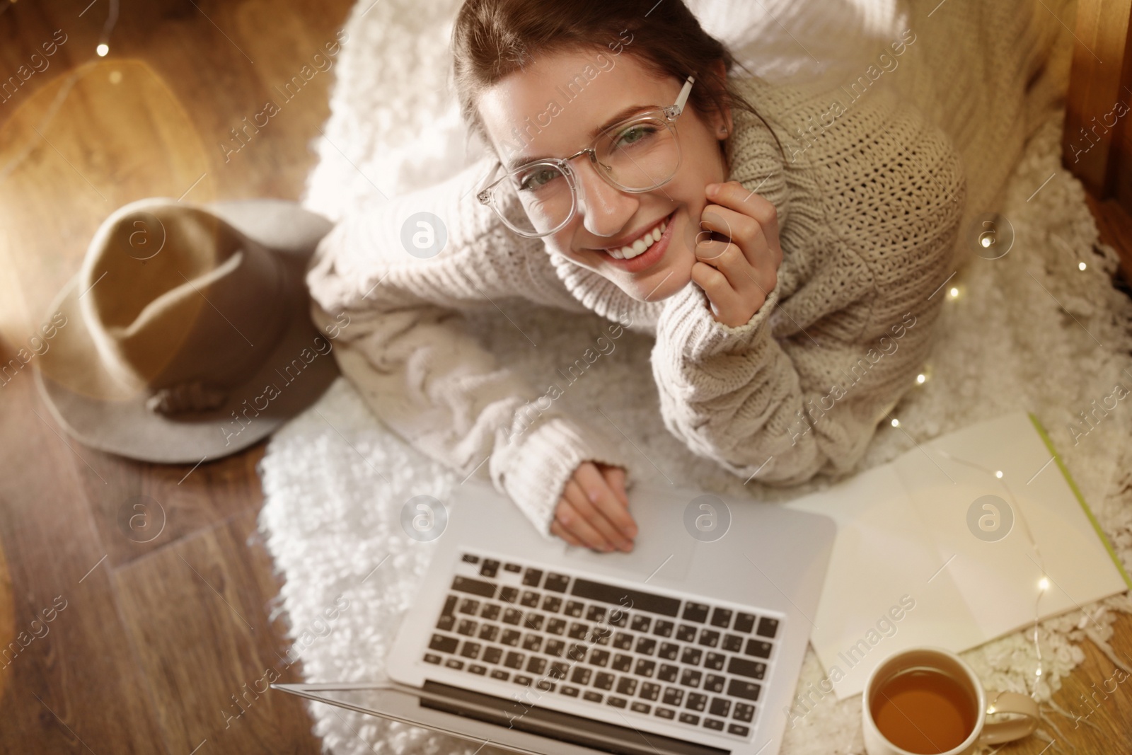 Photo of Woman with cup of hot beverage using laptop at home in winter evening