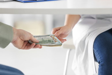 Photo of Patient giving bribe to doctor under table in clinic, closeup. Corrupted medicine