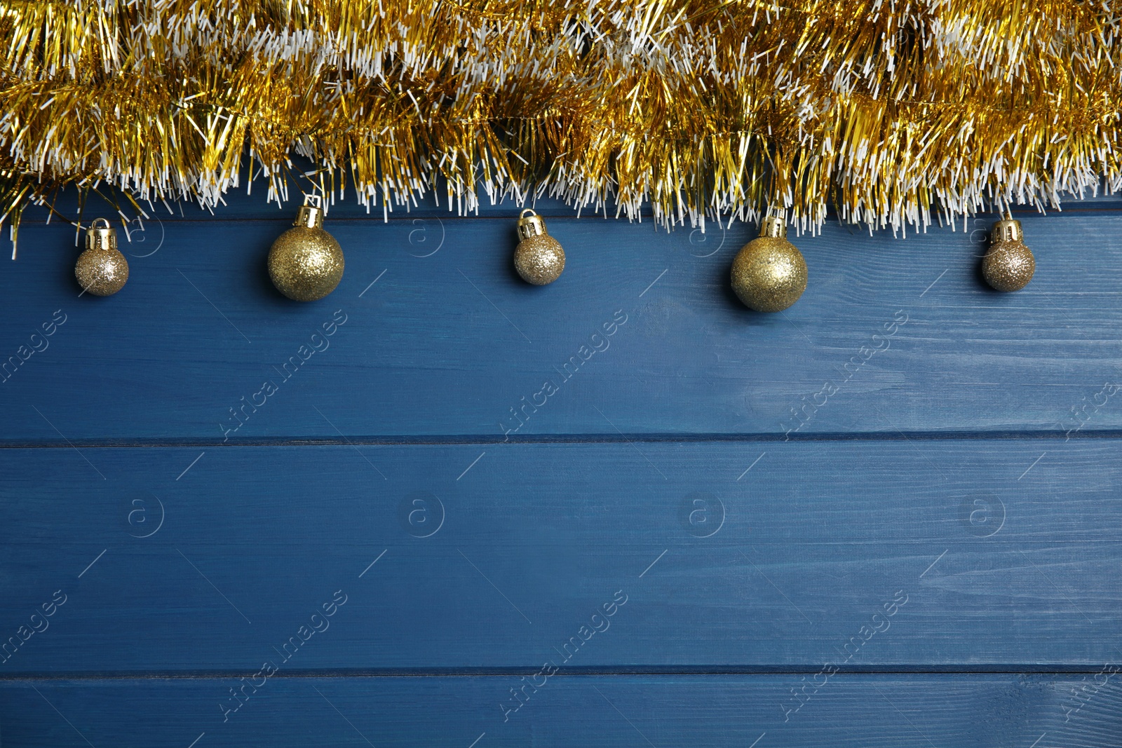 Photo of Golden tinsel and Christmas balls on blue wooden background, flat lay. Space for text