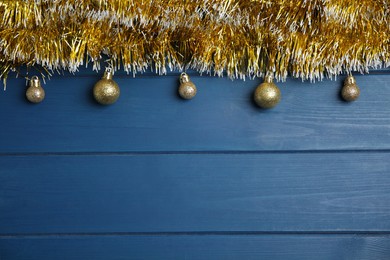 Golden tinsel and Christmas balls on blue wooden background, flat lay. Space for text