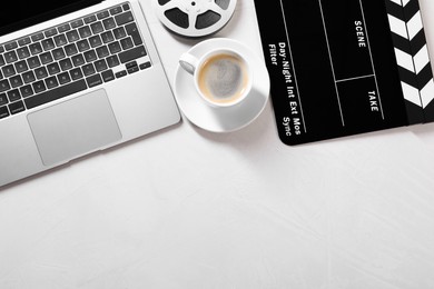 Movie clapper, film reel, laptop and coffee on light textured table, flat lay. Space for text