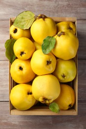 Tasty ripe quince fruits in crate on wooden table, top view