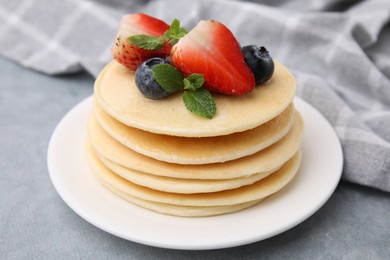 Photo of Stack of tasty pancakes with fresh berries, mint and honey on light grey table, closeup