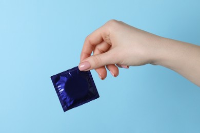 Woman holding condom on light blue background, closeup