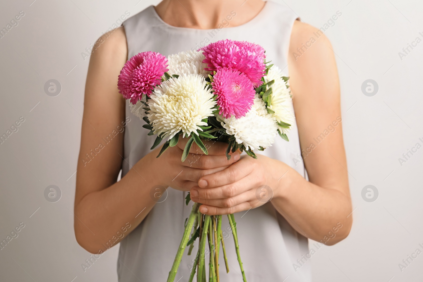 Photo of Woman holding beautiful aster flower bouquet against light background