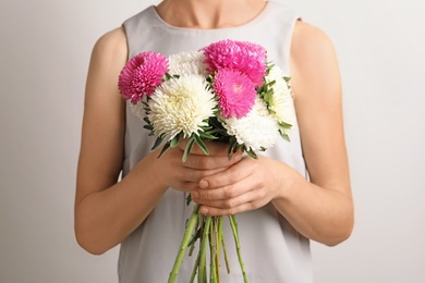 Woman holding beautiful aster flower bouquet against light background