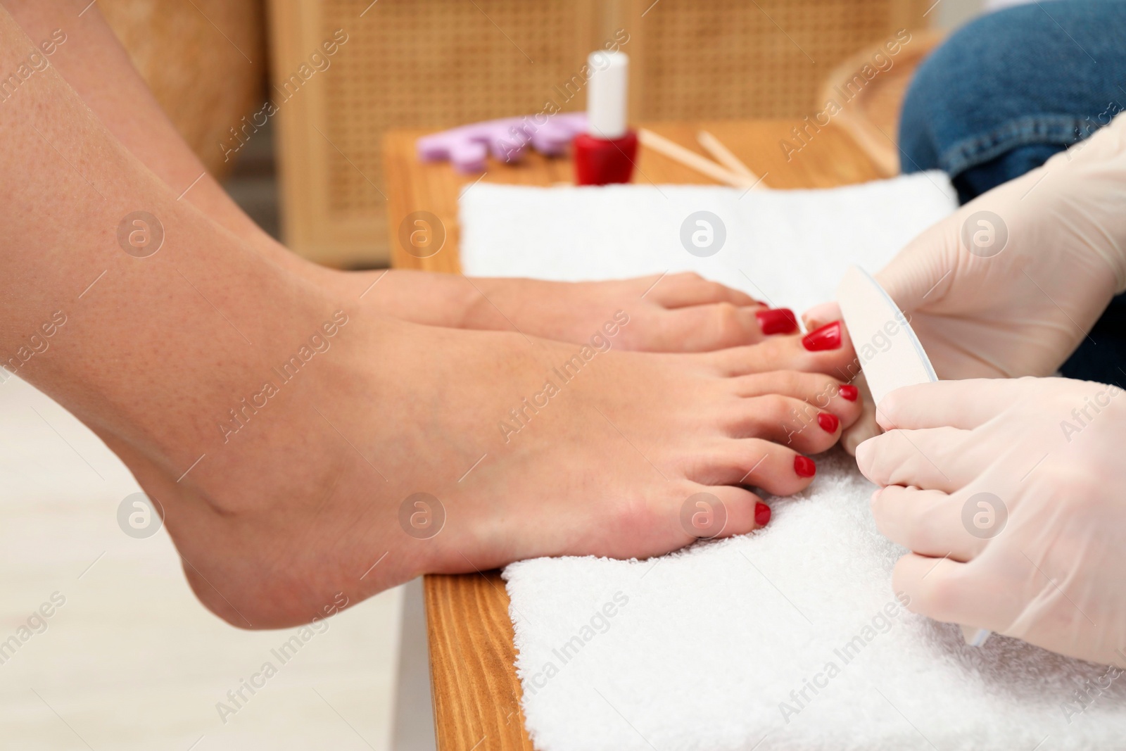 Photo of Pedicurist filing client`s toenails in beauty salon, closeup