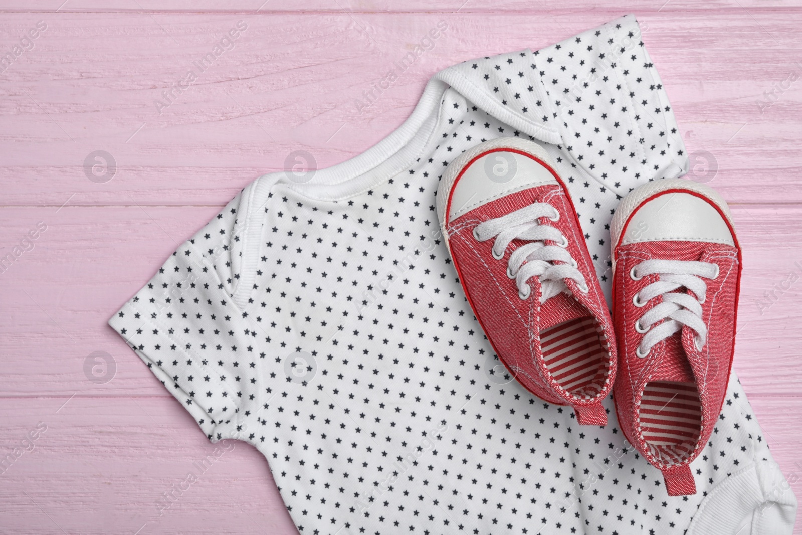 Photo of Child's romper and booties on pink wooden background, top view