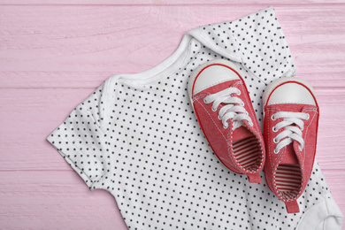 Child's romper and booties on pink wooden background, top view