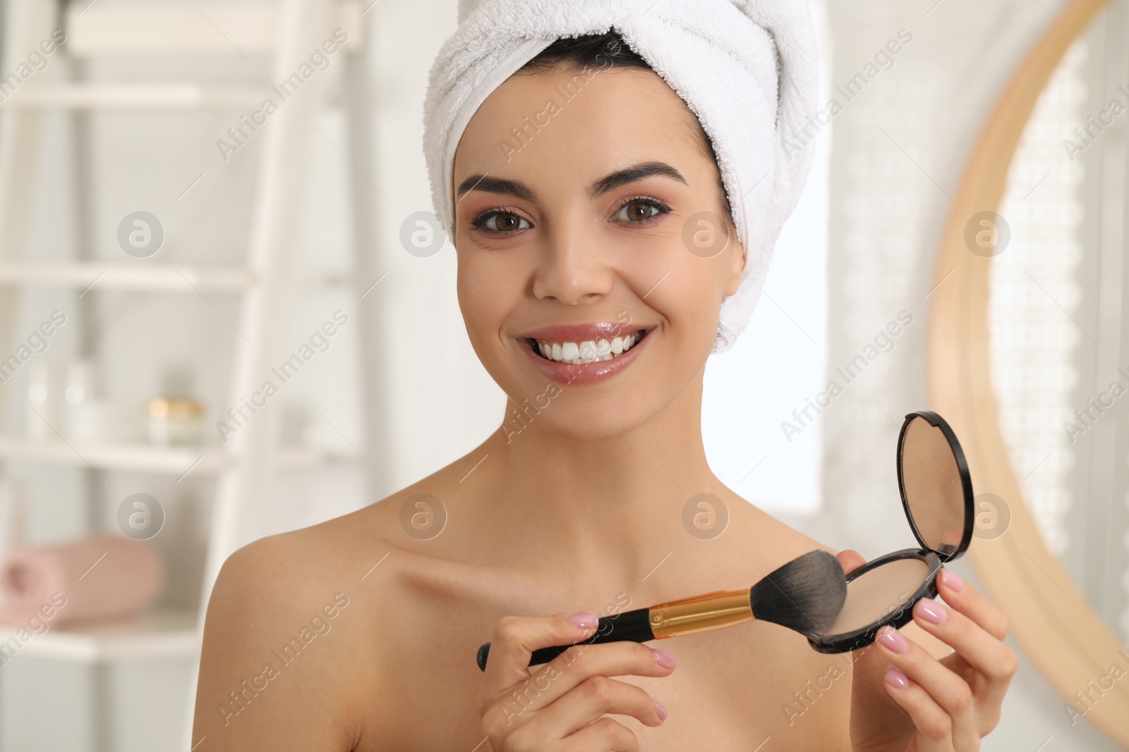 Photo of Beautiful young woman applying face powder with brush in bathroom at home