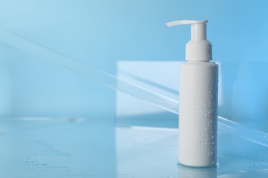 Photo of Wet bottle of face cleansing product on light blue background. Space for text