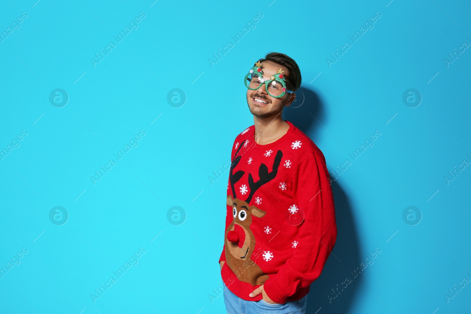 Photo of Young man in Christmas sweater with party glasses on color background