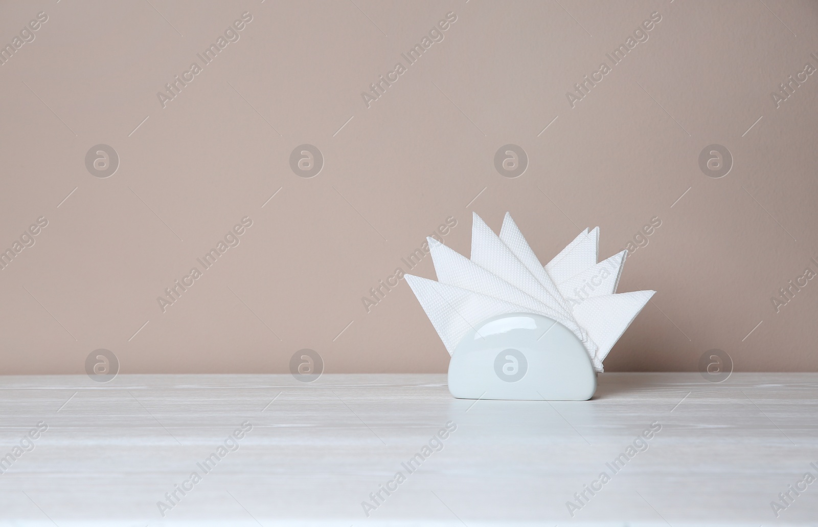 Photo of Napkin holder with paper serviettes on table against color background. Space for text