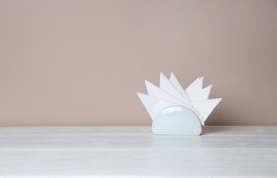 Photo of Napkin holder with paper serviettes on table against color background. Space for text