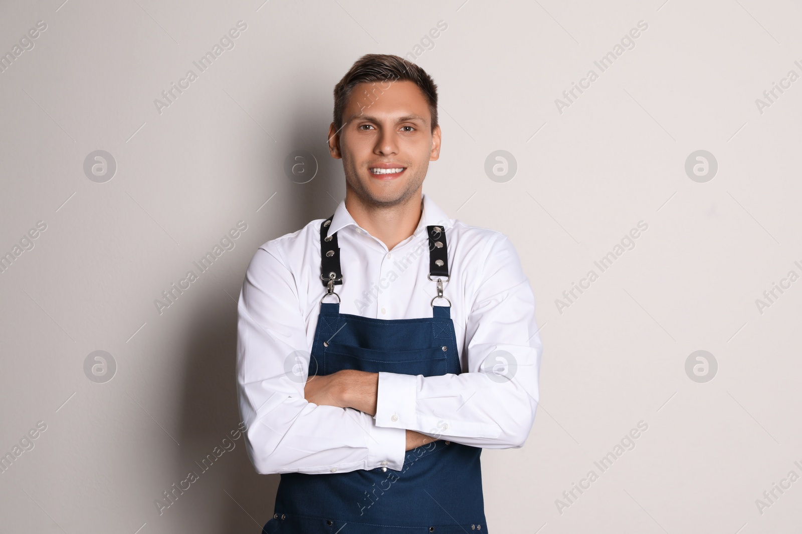 Photo of Portrait of happy young waiter in uniform on light background