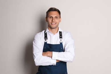 Portrait of happy young waiter in uniform on light background