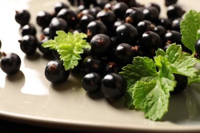 Photo of Ripe blackcurrants and leaves on plate, closeup