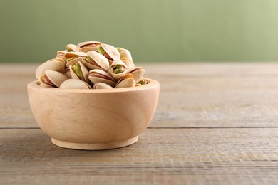 Photo of Tasty pistachios in bowl on wooden table against olive background, closeup. Space for text
