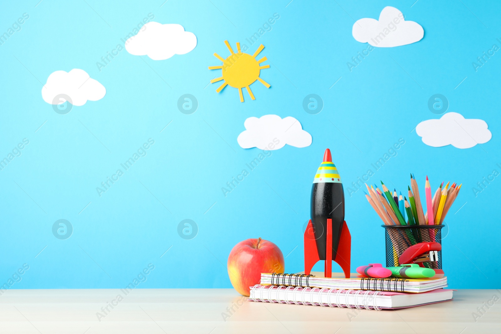 Photo of Bright toy rocket and school supplies on wooden table. Space for text