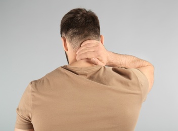 Young man suffering from neck pain on light background