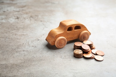 Wooden car model and coins on grey background. Space for text