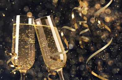 Glasses with sparkling wine and shiny serpentine streamers against blurred festive lights 