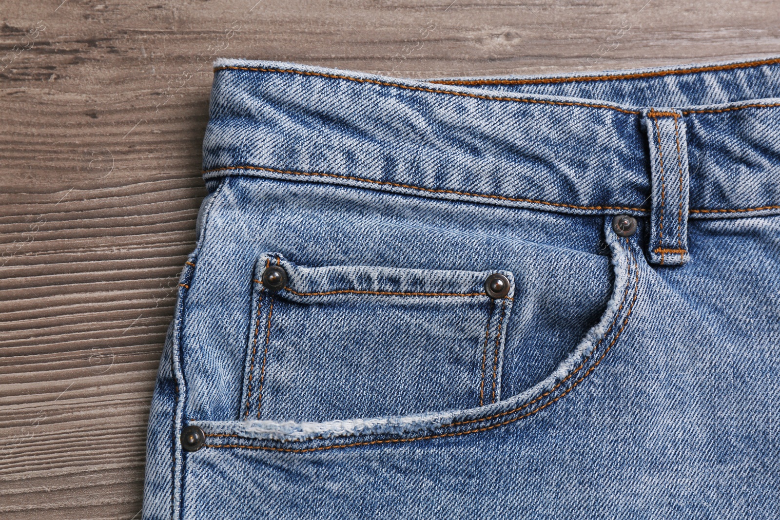 Photo of Stylish light blue jeans on wooden background, closeup of inset pocket