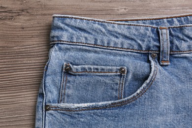 Stylish light blue jeans on wooden background, closeup of inset pocket