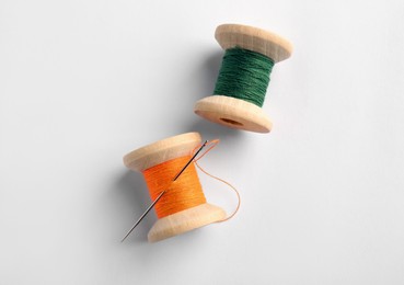 Colorful sewing threads with needle on white background, top view