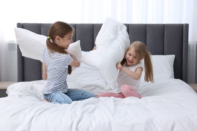 Photo of Cute little sisters having pillow fight on bed at home