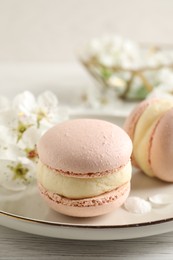 Photo of Delicious pink macarons and flowers on white wooden table, closeup