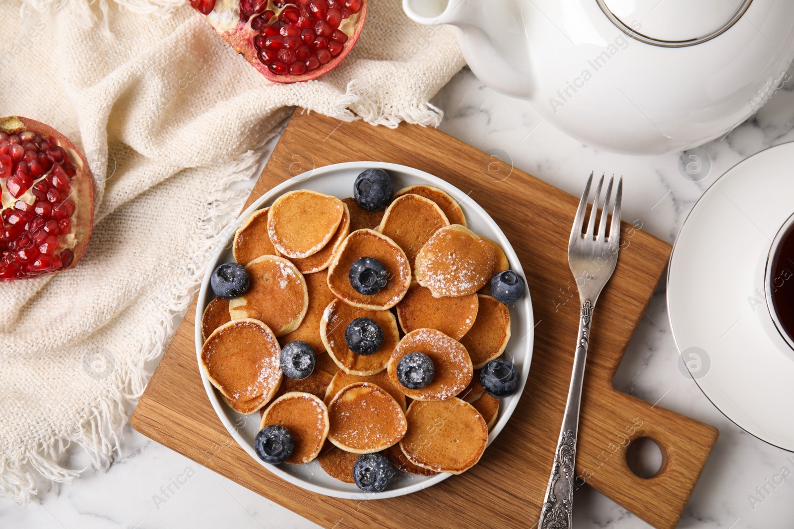 Photo of Delicious mini pancakes cereal with blueberries served on white marble table, flat lay