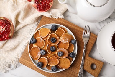 Photo of Delicious mini pancakes cereal with blueberries served on white marble table, flat lay